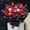 Bó hoa đỏ rực rỡ với hồng nhung, loa kèn đỏ, cẩm chướng được gói tinh tế trong giấy đen, thắt nơ "LOVE IS ETERNAL" tại STflo