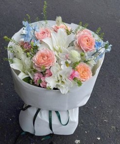 Bó hoa tươi thanh lịch với hoa hồng pastel, lily trắng và hoa điểm xuyết màu xanh biếc, gói trong giấy trắng tinh khôi, được
