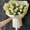 Bó hoa tulip trắng tinh khôi với giấy gói màu kem, được cầm bởi bàn tay một người tại STflowers