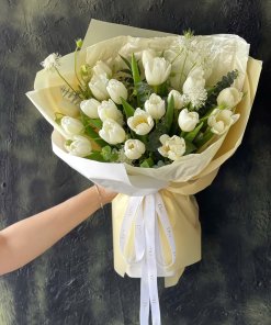 Bó hoa tulip trắng tinh khôi với giấy gói màu kem, được cầm bởi bàn tay một người tại STflowers