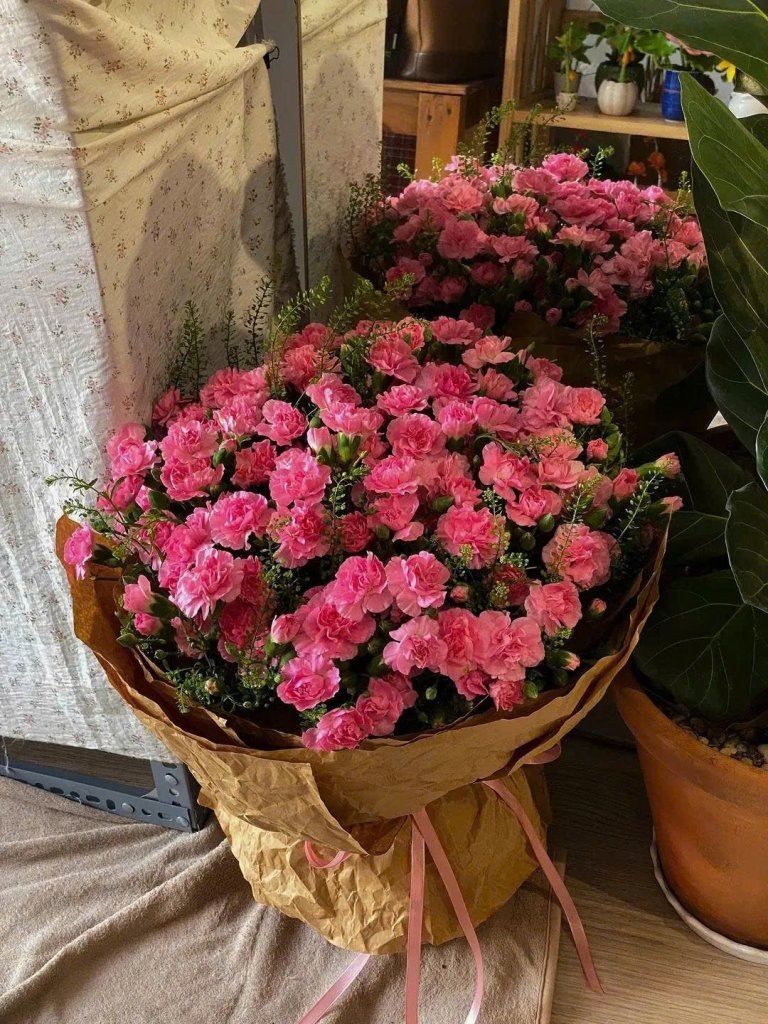 Bó hoa cẩm chướng màu hồng tươi thắm, dày đặc, được gói trong giấy nâu tại STflowers, Quận 7