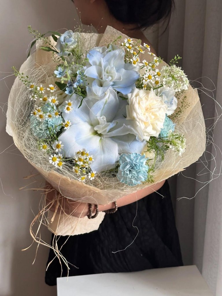 Bó hoa tươi với sắc xanh và trắng tinh tế, điểm xuyết cúc họa mi và lá xanh, được gói bằng giấy màu kem tự nhiên tại STflowe