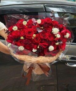 Bó hoa hồng đỏ rực rỡ sang trọng được gói cẩn thận, điểm xuyết hoa trắng nhỏ và lá phụ, thể hiện tình yêu nồng cháy. Đặt hoa