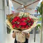 Bó hoa hồng đỏ tươi tắn, được gói giấy kraft và film trong suốt, tô điểm lá xanh, thể hiện tình yêu nồng nàn từ STflowers