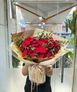 Bó hoa hồng đỏ tươi tắn, được gói giấy kraft và film trong suốt, tô điểm lá xanh, thể hiện tình yêu nồng nàn từ STflowers
