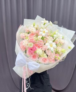 Bó hoa tươi tone hồng pastel và trắng, gói giấy sang trọng với nơ trắng lớn, trang trí ruy băng, của STflowers tại Quận 7, TP.HCM.