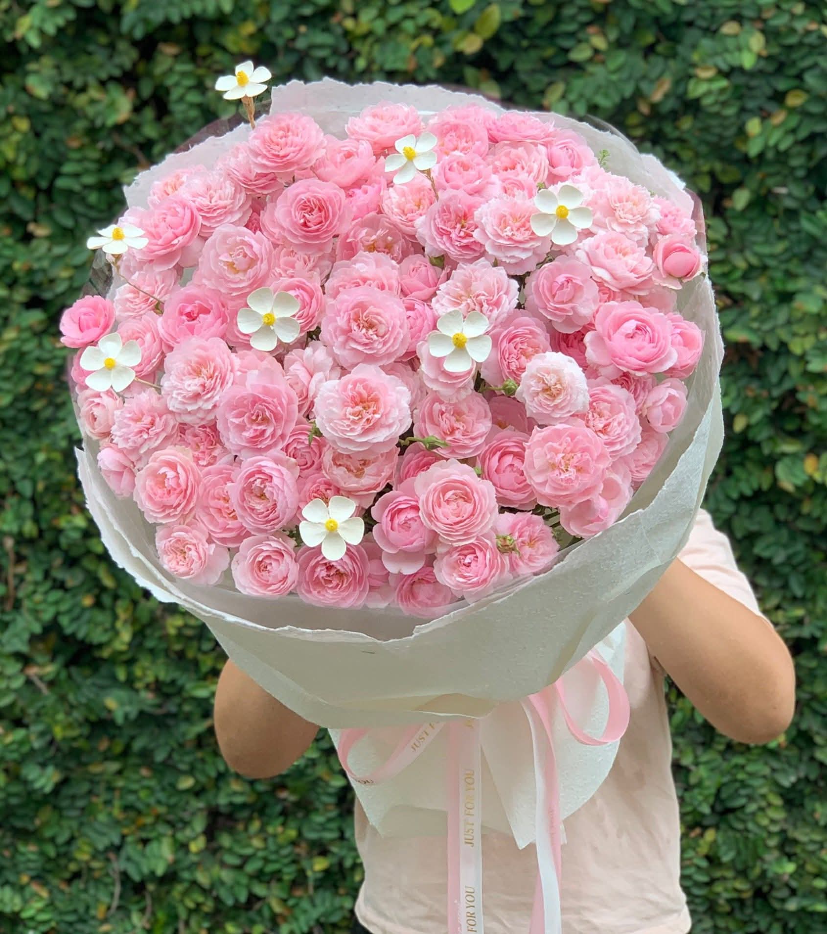 Một bó hoa hồng phấn lớn, thanh lịch được gói giấy trắng tinh tế, điểm xuyết hoa nhỏ trắng, đang được STflowers cung cấp tại TP.HCM.