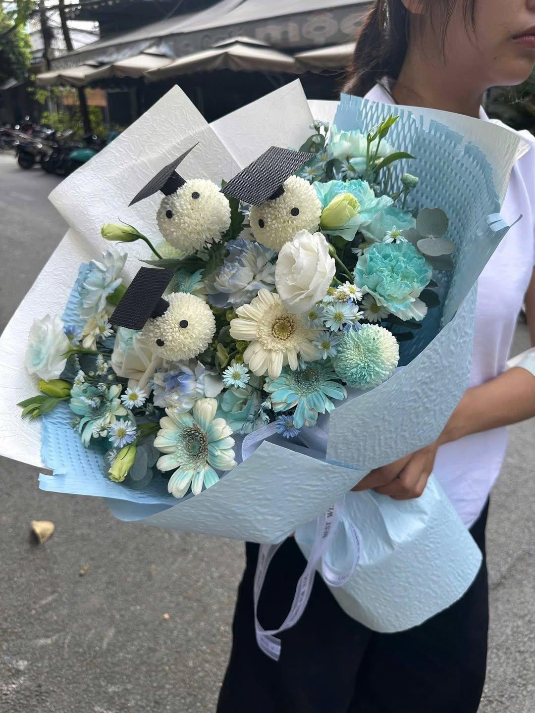 Bó hoa tốt nghiệp xanh trắng tươi tắn từ STflowers, với các bông hoa trắng đội mũ cử nhân và hoa tươi tone xanh dịu dàng.